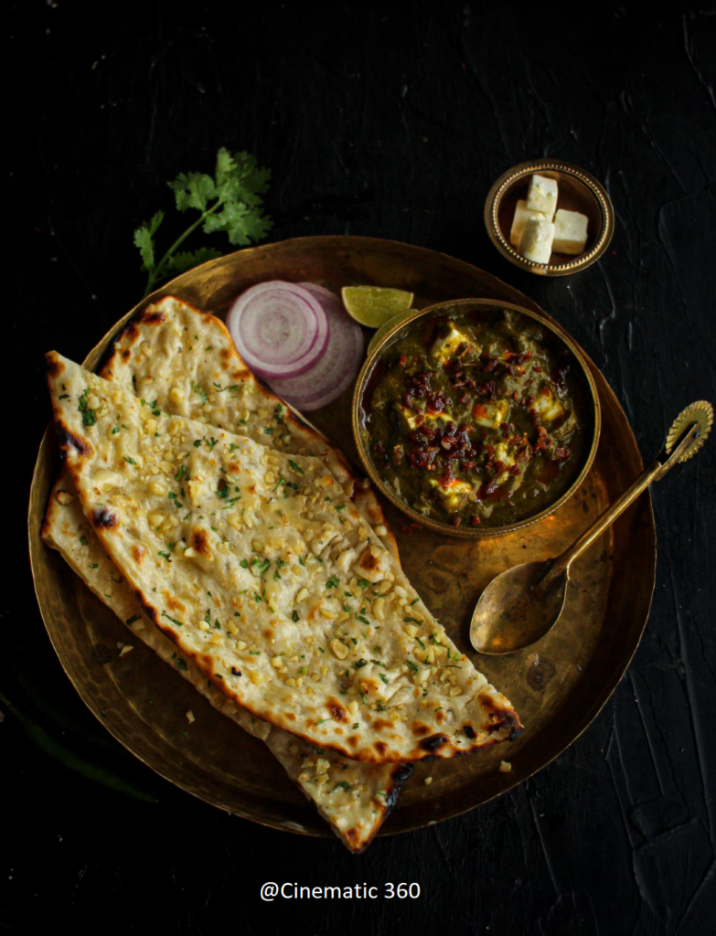 Dark and moody overhead flat lay food photography of rich Palak Paneer served with butter garlic naan on an antique brass thali by Cinematic360.