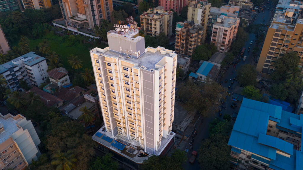 Aerial drone shot of a modern high-rise residential building by Jaliyan Group in Mumbai, captured at golden hour, showcasing premium real estate architecture, elevation mapping, and urban density for a developer launch blueprint.