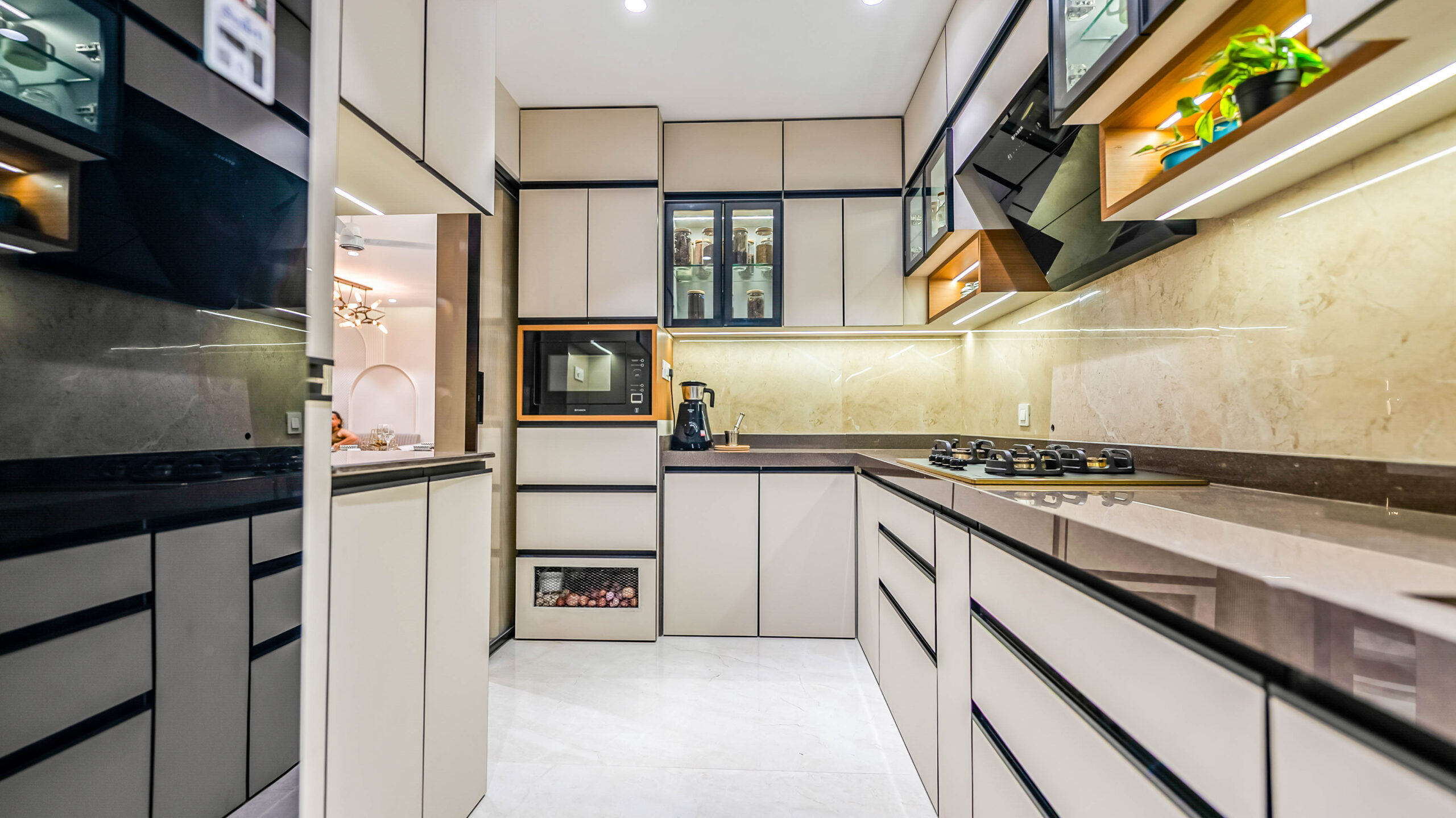 A spacious U-shaped kitchen layout featuring high-gloss beige cabinetry, granite countertops, and smart storage solutions including a wicker vegetable basket and glass display shelves.
