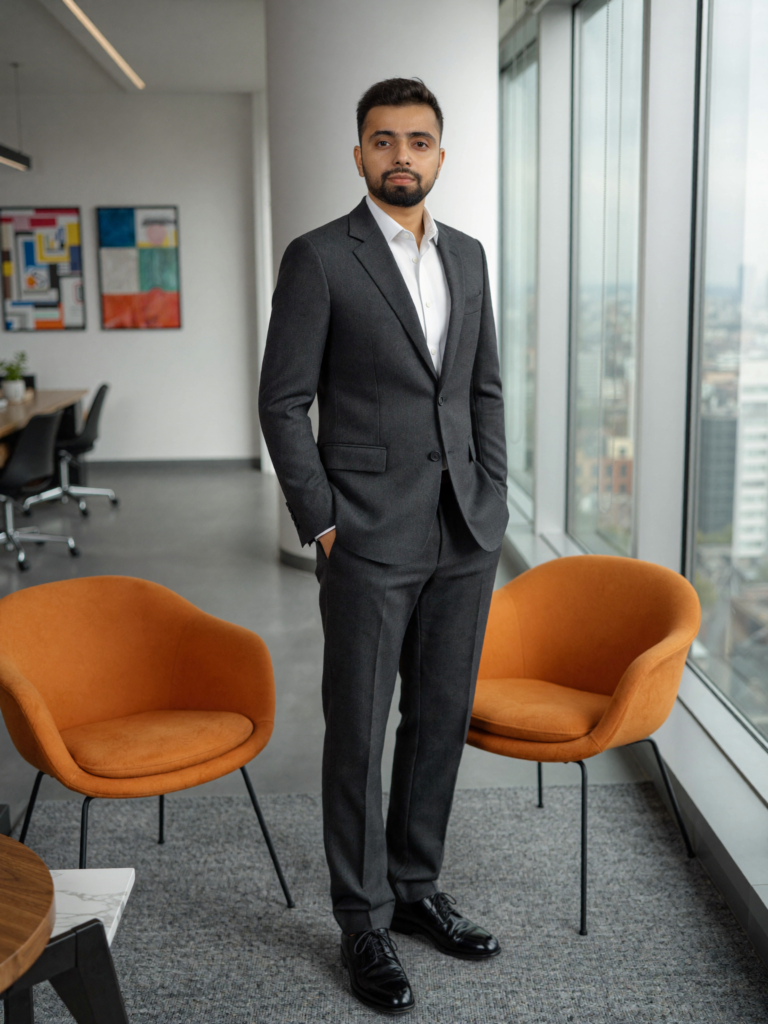 Deepankar kumar in a dark business suit standing near large floor-to-ceiling glass windows inside a modern office with orange lounge chairs and natural daylight.