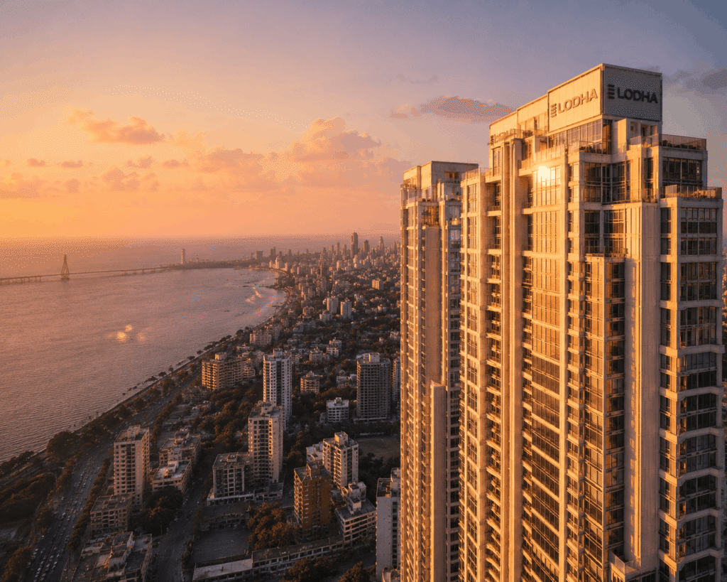Drone view of a luxury Mumbai high-rise overlooking the Arabian Sea with warm sunset light and city skyline in the background.