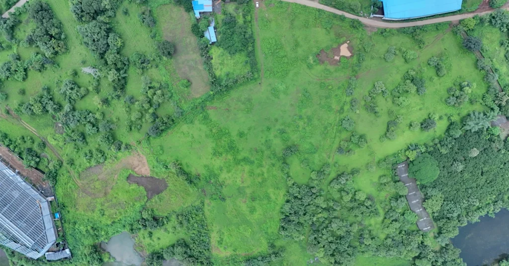 Top-down aerial drone photograph of a vacant commercial land plot for real estate development in Bhiwandi, Mumbai, showcasing green fields, surrounding access roads, and boundary mapping for a developer's pre-launch site blueprint.