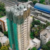 erial drone photograph tracking the structural progress of a high-rise tower under construction in Mumbai next to a railway line, featuring a graphic annotation highlighting the 15th floor and scaffolding setups by Cinematic360.