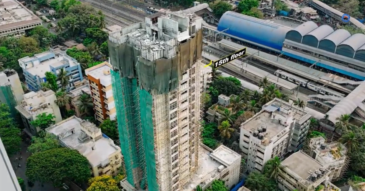 erial drone photograph tracking the structural progress of a high-rise tower under construction in Mumbai next to a railway line, featuring a graphic annotation highlighting the 15th floor and scaffolding setups by Cinematic360.
